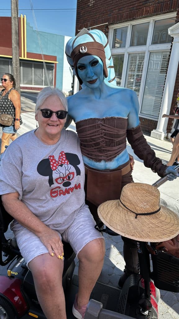 Person dressed as a Star Wars character posing with an older woman on a scooter in downtown Panama City on Star Wars event week