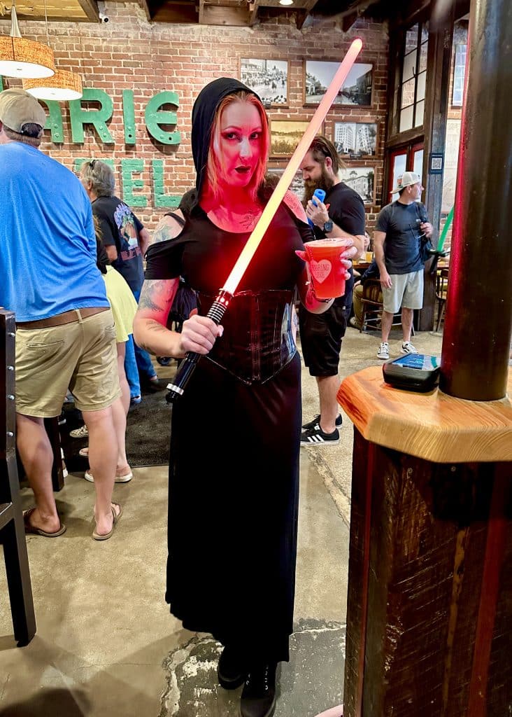 Woman dressed as a character from Star Wars holding a beer and light saber at History Class Brewing in downtown Panama City on Star Wars Day